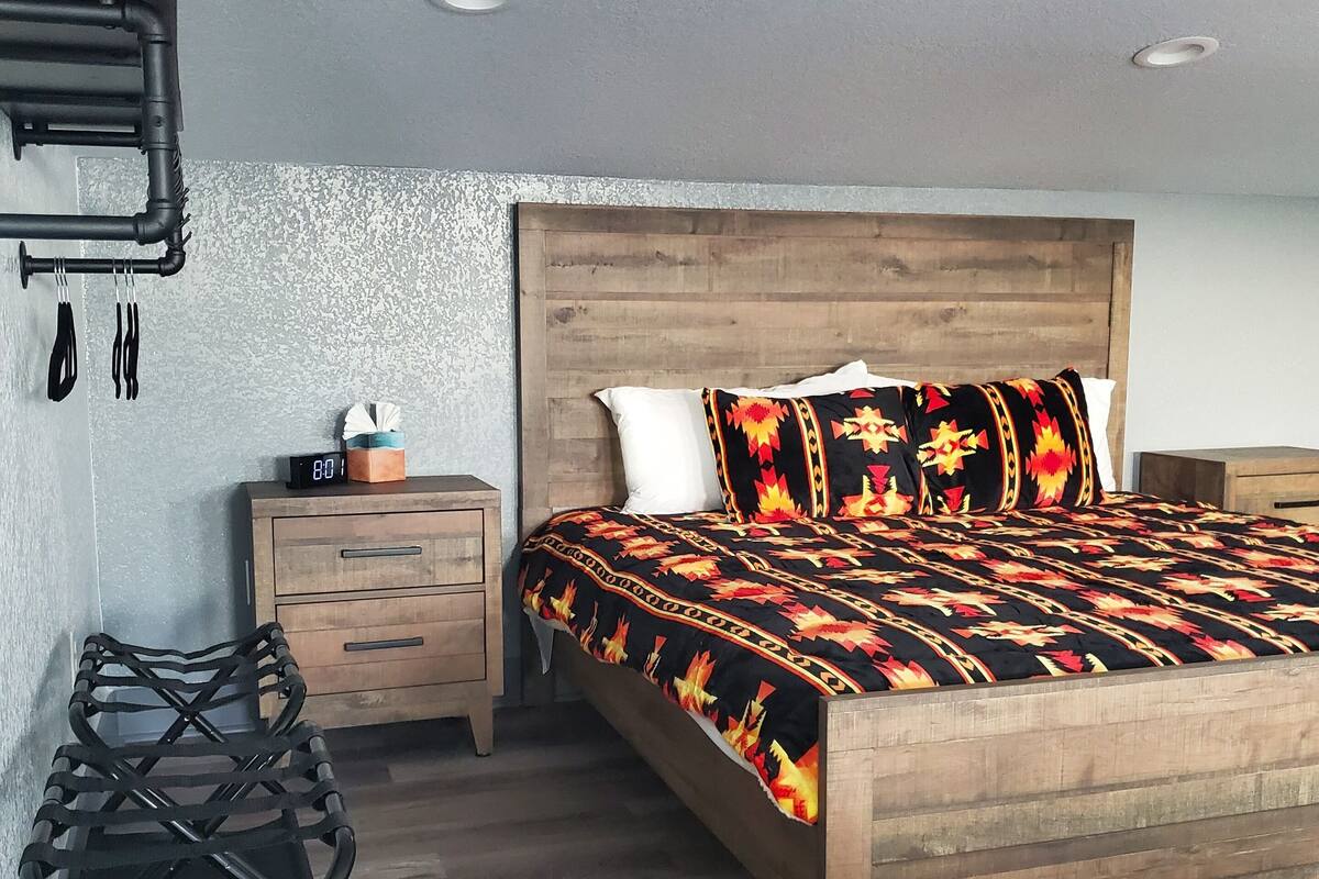 Ein Schlafzimmer mit einem hölzernen Bett, einem Nachttisch, einem schwarzen Stuhl und einem Wandregal mit Utensilien.