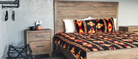 A bedroom with a wooden bed, a nightstand, a black chair, and a wall-mounted shelf with utensils.