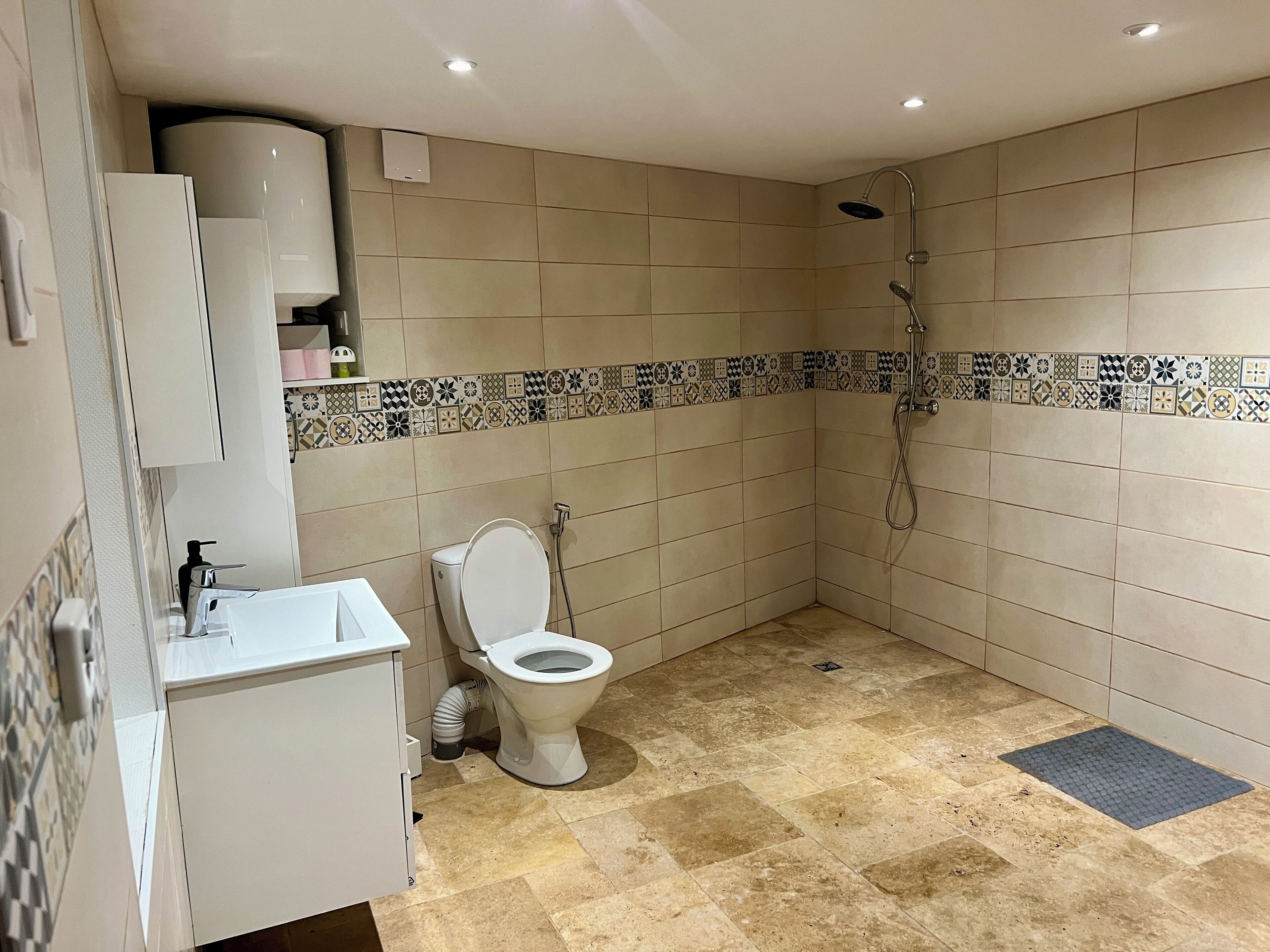 Un baño con inodoro, lavamanos, ducha y paredes con azulejos.