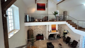 Rummelig indretning med højt til loftet, en stenvægspejs og en trappe til en etage over.