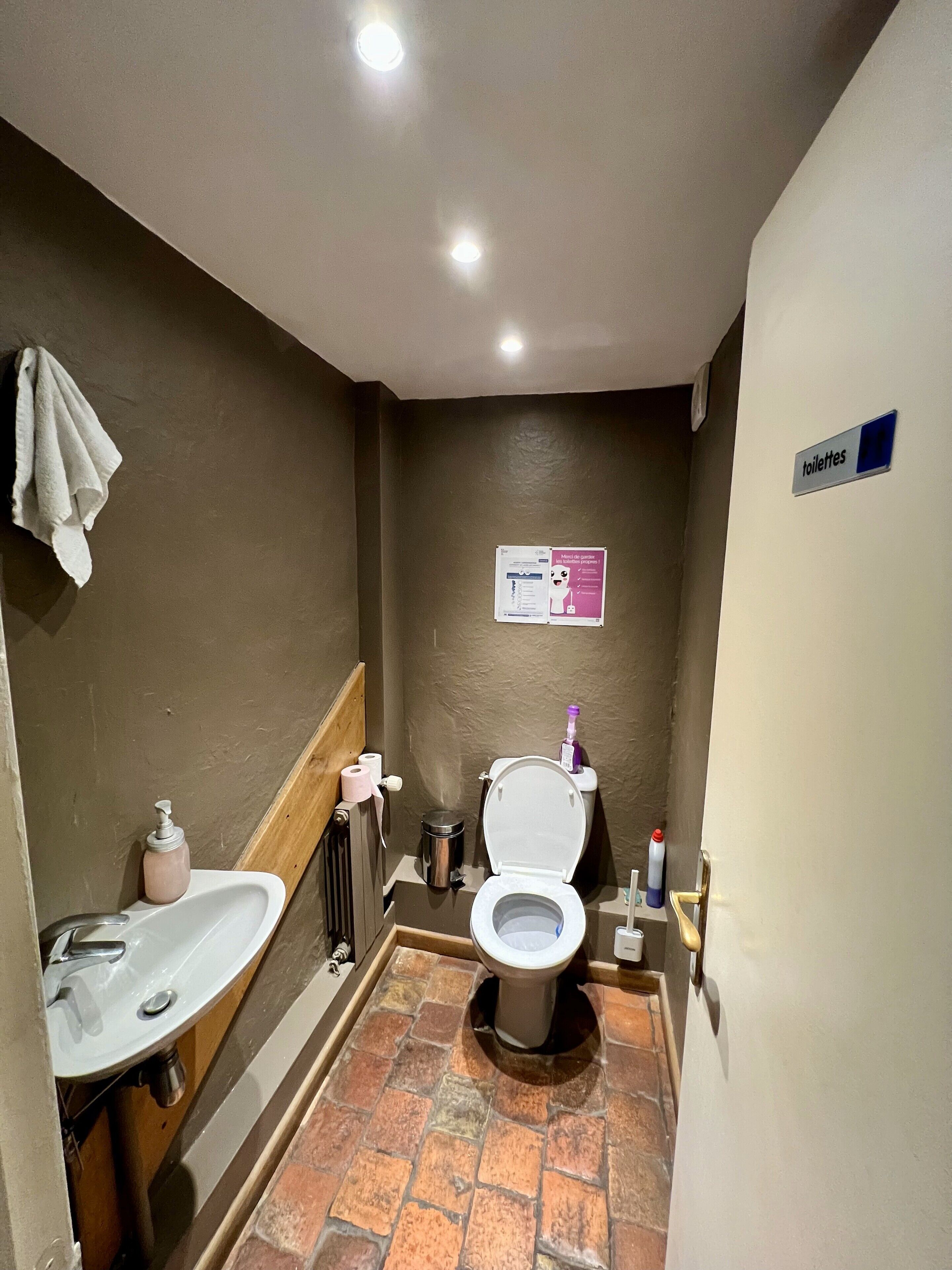 A small bathroom with a toilet, sink, and a sign indicating the location of toilets.