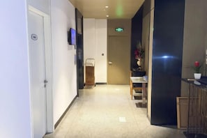 Un pasillo de hotel con una recepción, un televisor y una puerta con letrero de salida de emergencia.