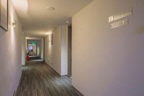 Un pasillo de hotel con señales de orientación, piso alfombrado y extintor.