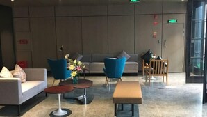 En moderne lobby med en sofa, blå stole, en træstol, et lille bord med blomster og en bænk.
