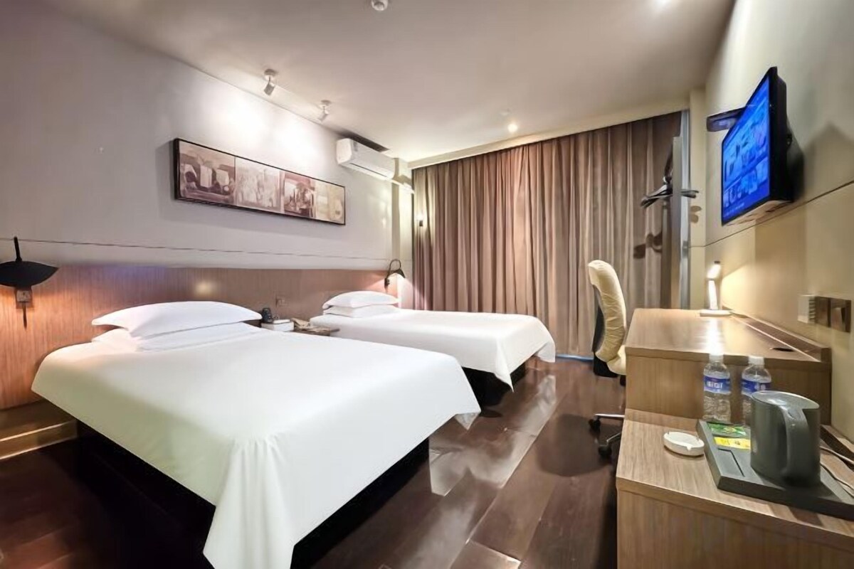 Quarto de hotel com duas camas, uma escrivaninha com computador, televisão e uma janela grande com cortinas.