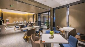 En moderne hotellobby med forskellige siddepladser, herunder borde og stole, samt et receptionområde med disk og planter.