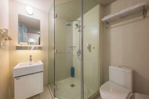 Ett badrum med en dusch som är avskärmad med glasväggar, ett vitt handfat och en toalett.