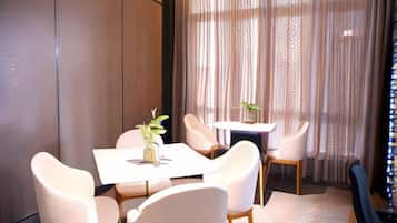 A dining area with a table and chairs, a vase with a plant, and a view through sheer curtains.