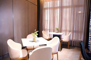 A dining area with a table and chairs, a vase with a plant, and a view through sheer curtains. - Jinjiang Inn Select (Wenzhou High-speed Railway Station Xinqiao) (Wenzhou)