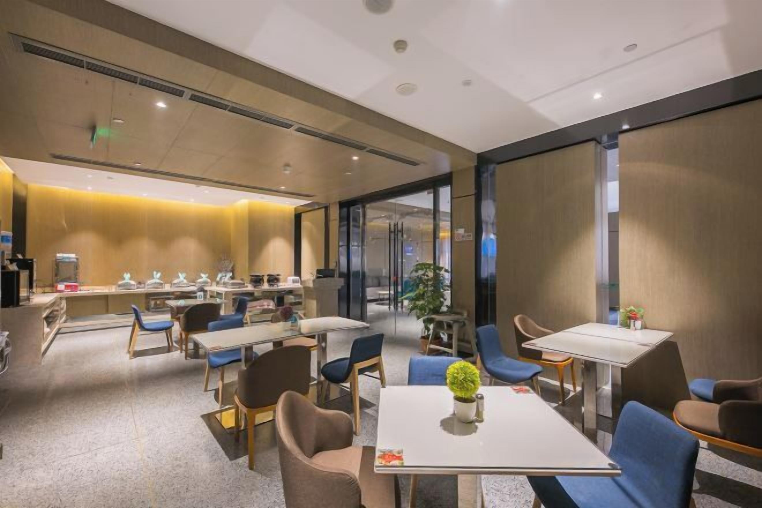 A modern hotel dining area with tables and chairs, a bar area, and a large window providing natural light.