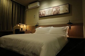 Ett hotellrum med en stor säng, två sänglampor, en väggmonterad luftkonditioneringsanläggning och en inramad tavla ovanför sängen.