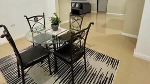 A dining area with a glass table and metal chairs, a black and white rug, and a kitchen in the background. - The Unico Vacation Villa (st Ann)