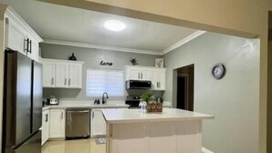 A modern kitchen with white cabinetry, a central island, and a built-in microwave. - The Unico Vacation Villa (st Ann)