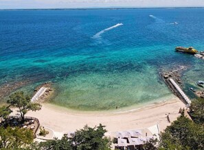 Een strand met helder turquoise water, een zandstrand en een steiger met boten.