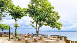 Un área de comedor al aire libre con mesas y sillas, con vista a un cuerpo de agua.