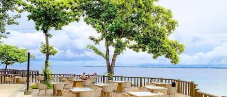Un área de comedor al aire libre con mesas y sillas, con vista a un cuerpo de agua.