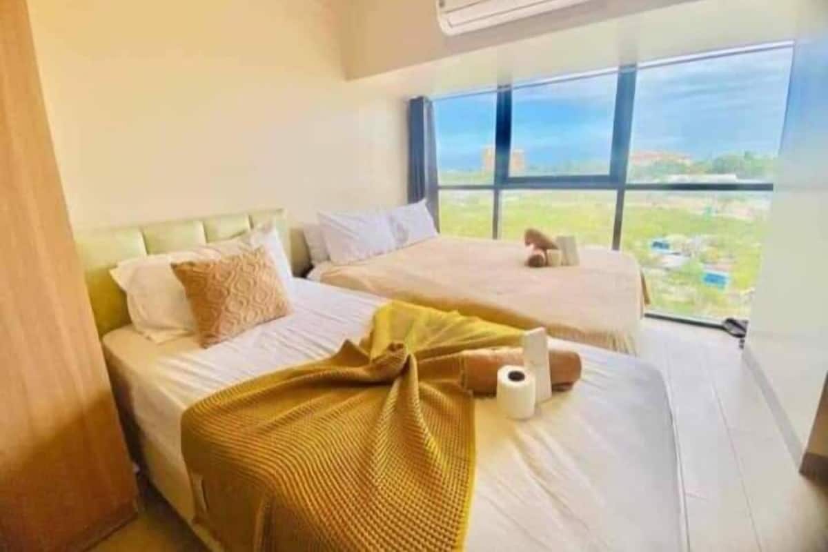Ein Hotelzimmer mit zwei Betten, einem großen Fenster mit Blick auf die Stadt und einer Klimaanlage an der Wand.