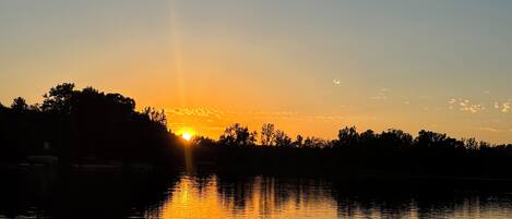A sunset over a calm body of water with a silhouette of trees and a distant building.