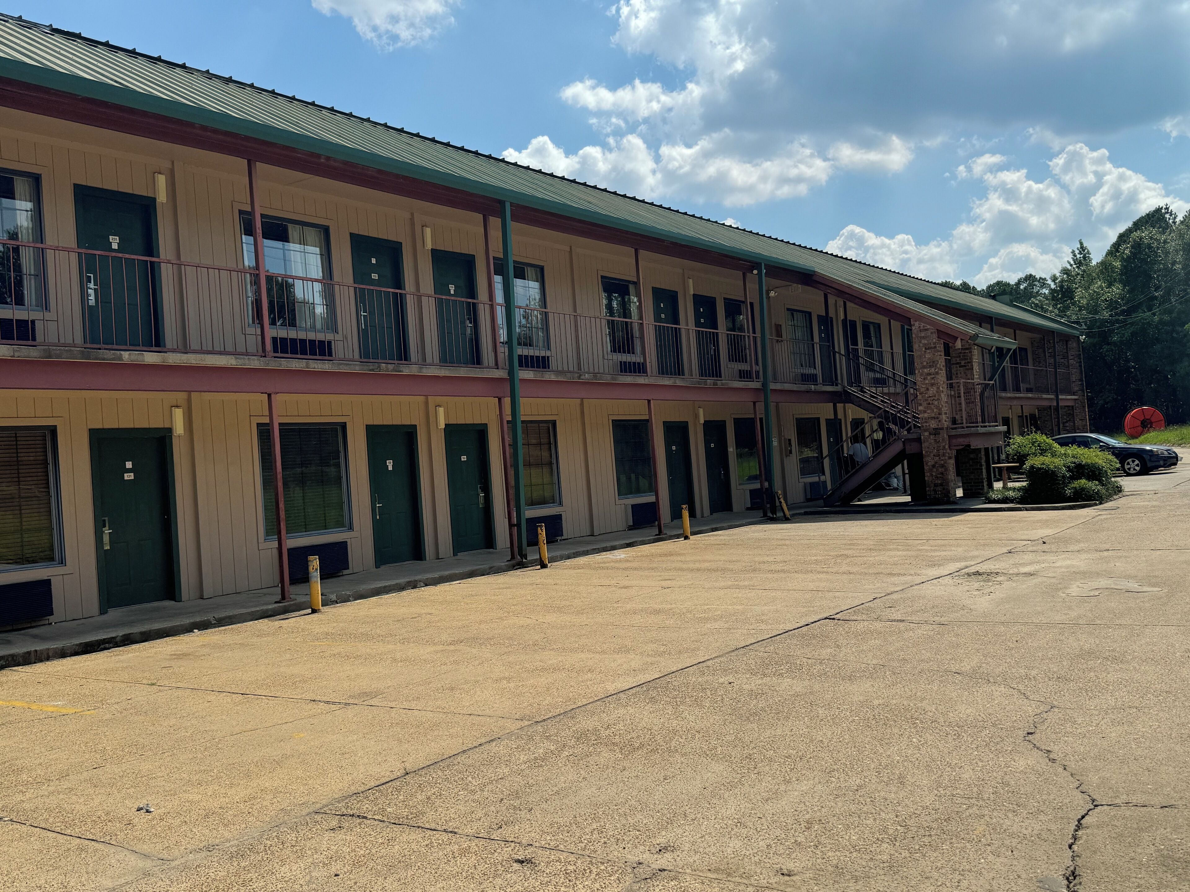 A motel with multiple rooms, a covered parking area, and a staircase leading to an upper level.