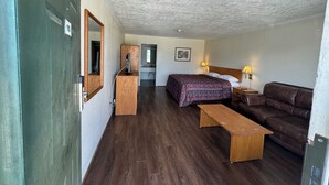 A hotel room with a bed, a bench, a sofa, a desk with a computer, a mirror, and a door.
