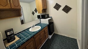 A bathroom with a sink, wooden cabinets, a mirror, a coffee maker, and decorative wall pieces. - Country Inn (Leesville)