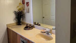 A bathroom with a beige sink, a mirror, and a vase with yellow flowers. - Country Inn (Leesville)