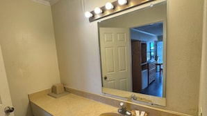 A bathroom with a beige vanity, a sink, a mirror with lights, and a door.