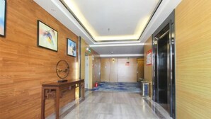 Eine Hotelhalle mit Holzvertäfelung, einem Empfangstresen, einem großen Spiegel und einem modernen Aufzug.