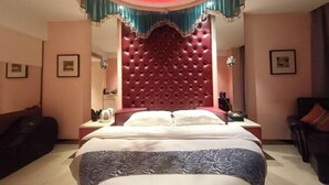 Ein Hotelzimmer mit einem großen Bett, einem roten, gepolsterten Kopfteil, einem Nachttisch, einem Schreibtisch und einem Stuhl.