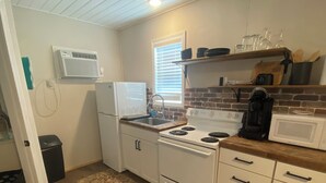 A compact kitchen with white cabinetry, a stove, a microwave, and a window with blinds. - Pet friendly cabin in quiet Plainview with WiFi, AC (Plainview)