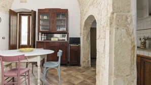 A dining area with a white table, two chairs, a wooden cabinet, and a television. - Appartamento Vintage con Balcone by Wonderful Italy (Ostuni)