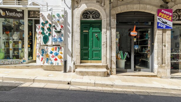 A street with shops, including a green door entrance and a sign for a fish shop. - Appartamento Vintage con Balcone by Wonderful Italy (Ostuni)