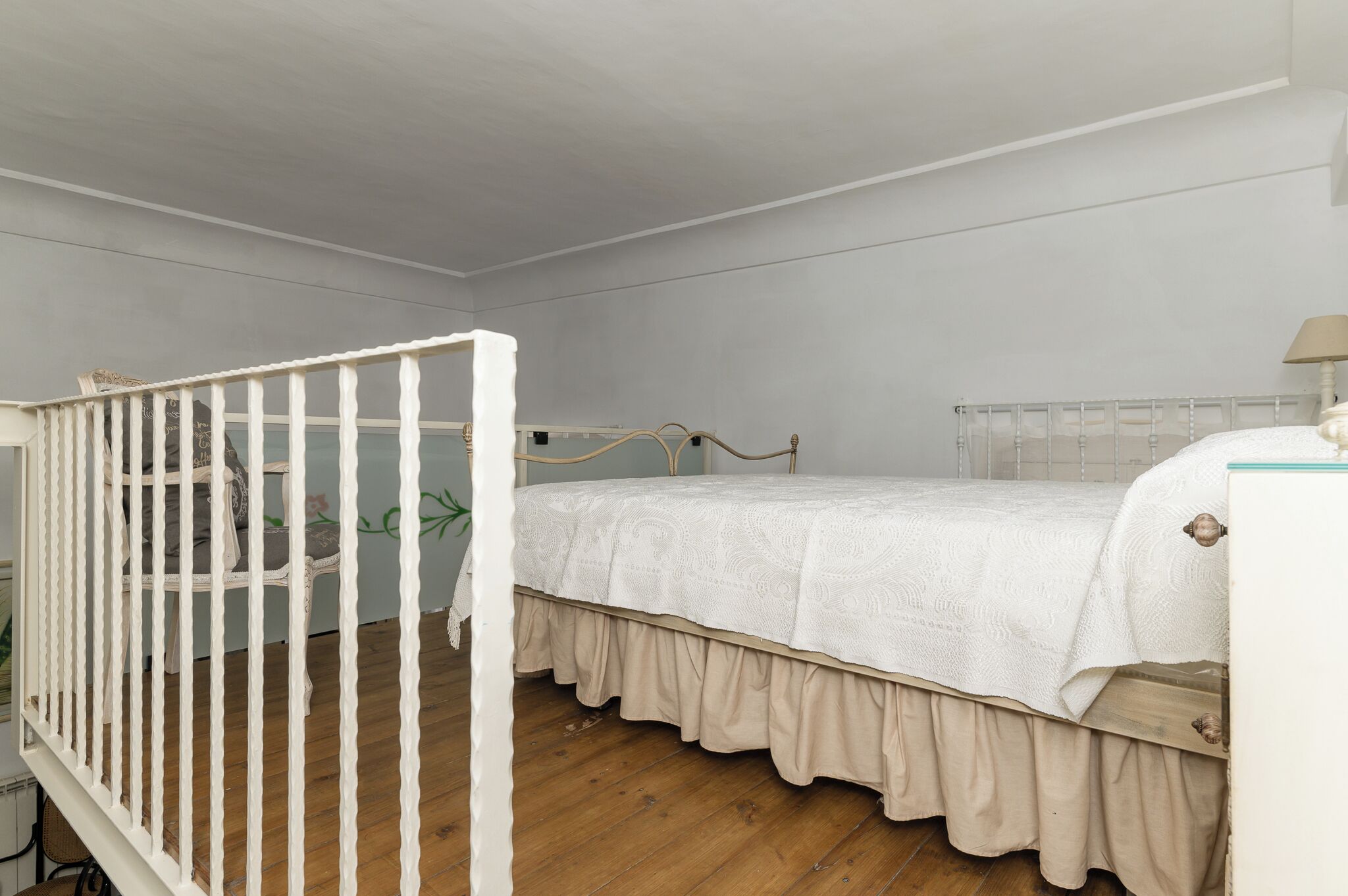 A bedroom with a white crib, a bed with a white bedspread, and a wooden floor.