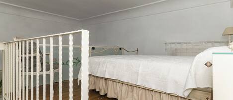 A bedroom with a white crib, a bed with a white bedspread, and a wooden floor.
