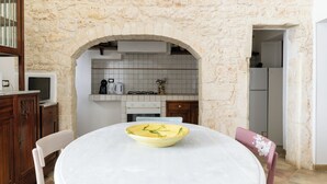 A dining area with a round table, a yellow bowl, and a stone wall. - Appartamento Vintage con Balcone by Wonderful Italy (Ostuni)
