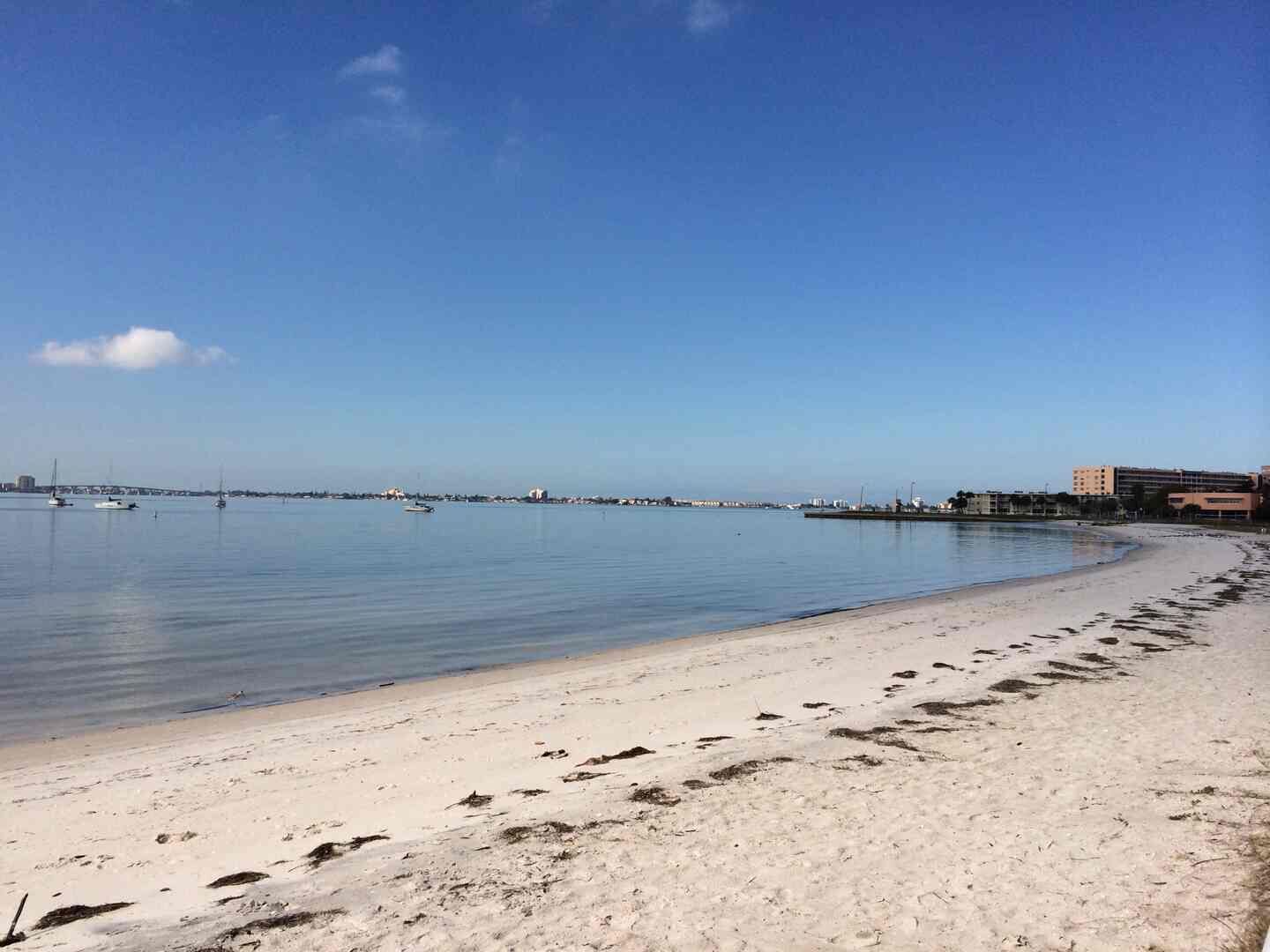 A beach with a clear sky, calm water, and footprints leading to the shore.