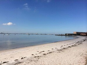 Une plage avec un ciel dégagé, une eau calme et des empreintes de pas qui mènent au bord de l’eau.
