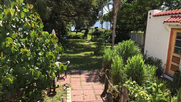 A paved pathway leading to a house with a red-tiled roof, surrounded by lush greenery and a small garden. - Waterfront Gulfport Studio w/Shared Private Beach + Walk to Beach & Dining (Gulfport)