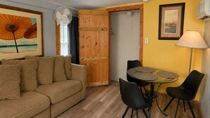 A cozy living area with a sofa, a dining table with chairs, a fan, and a door leading to another room. - Waterfront Gulfport Studio w/Shared Private Beach + Walk to Beach & Dining (Gulfport)