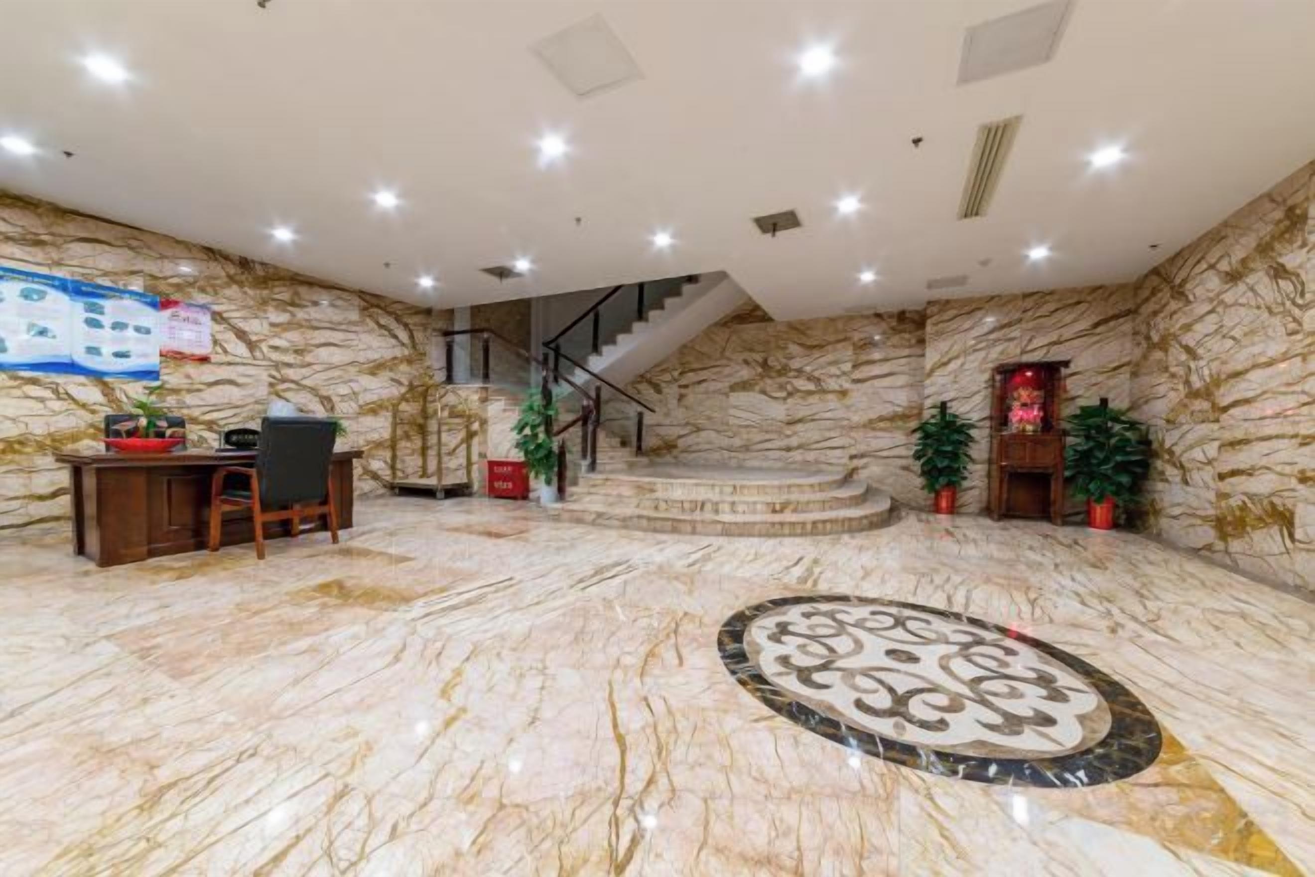 Un hall con suelo de mármol, un mostrador de recepción, una escalera y plantas en macetas.