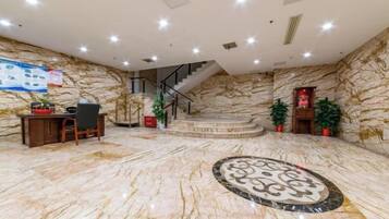 Un hall con suelo de mármol, un mostrador de recepción, una escalera y plantas en macetas.