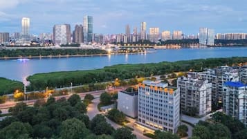 A modern high-rise building with a flat roof and a rectangular shape, surrounded by greenery and a river.