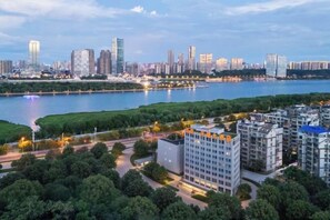 A modern high-rise building with a flat roof and a rectangular shape, surrounded by greenery and a river. - Handsome Tianlu Hotel (Changsha)