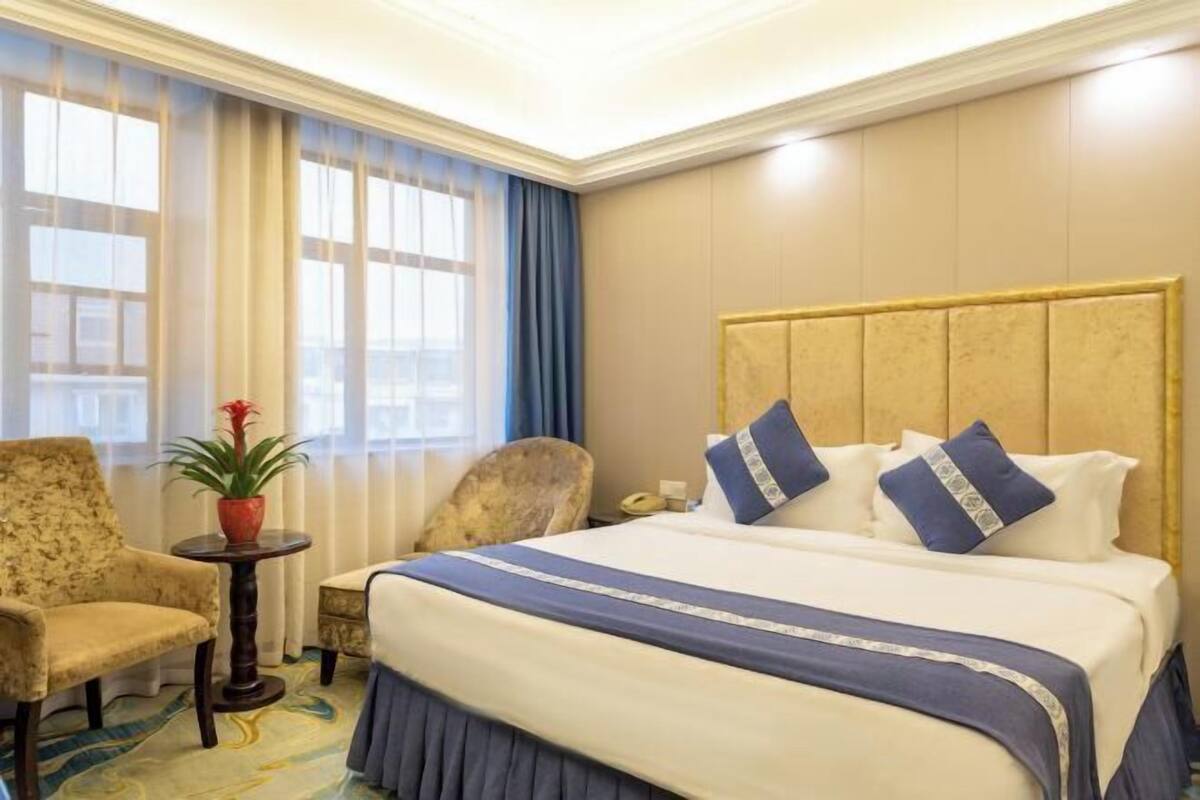 Hotellihuone, jossa on suuri sänky, tuoli, pieni pöytä ja ruukussa oleva kasvi.