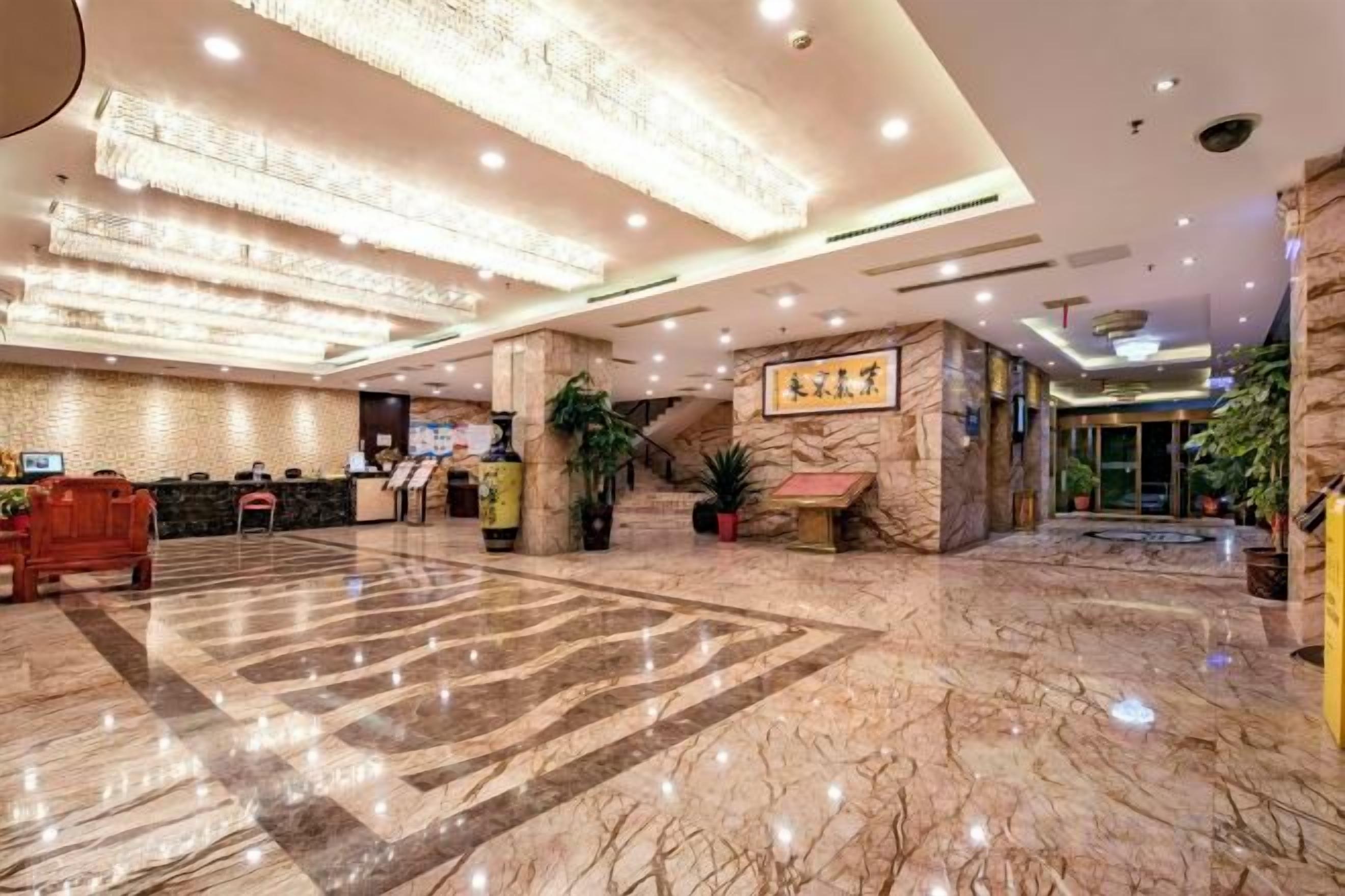 Un vestíbulo de hotel con piso de mármol, una recepción y una escalera que conduce a un nivel superior.