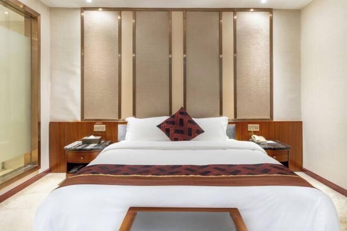Hotellihuone, jossa on suuri sänky, puinen pääty, yöpöydät ja näkymä lasiovesta.
