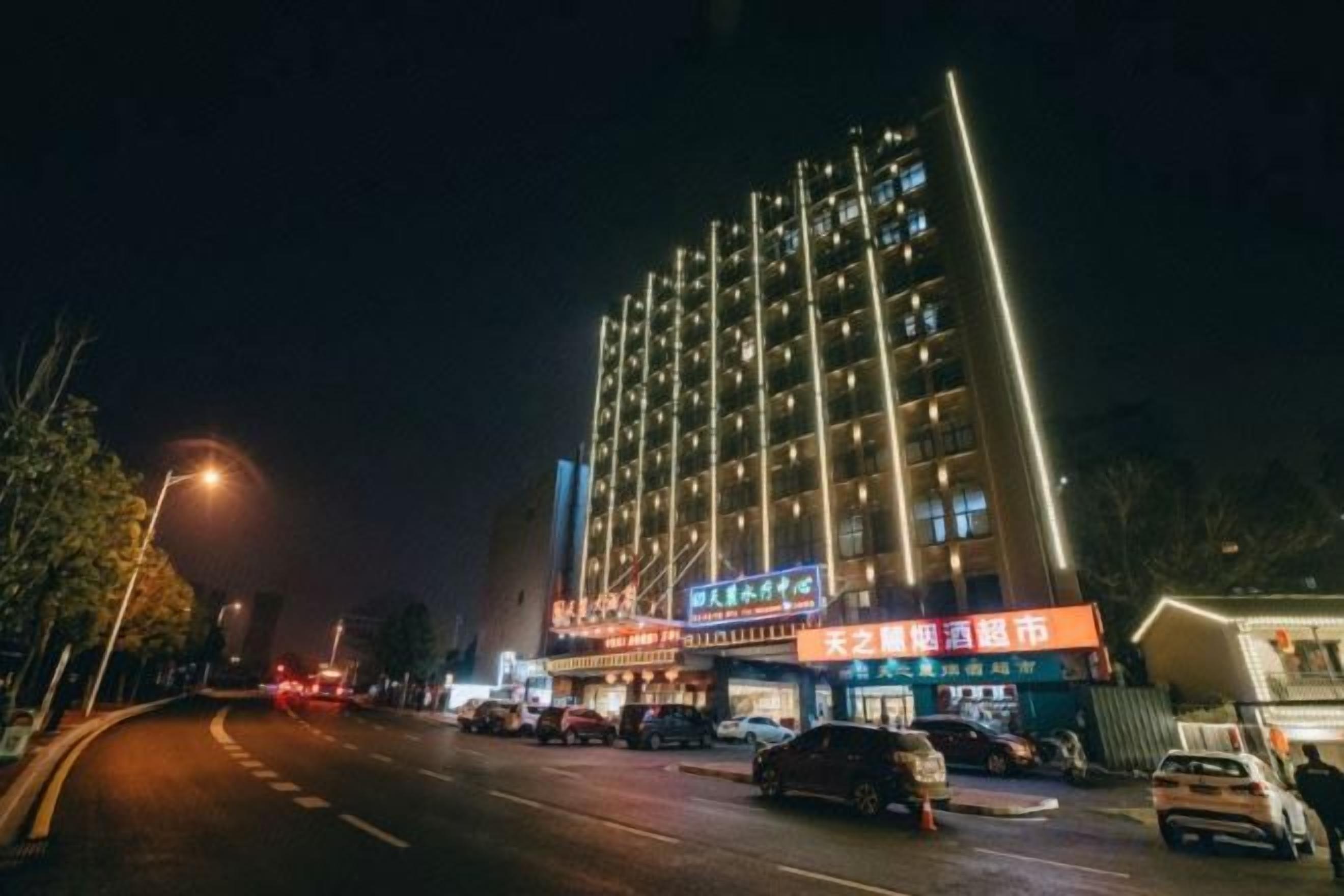 Un hotel de varios pisos con señalización iluminada, un estacionamiento y vista a la calle.