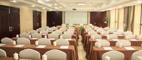A conference room with rows of tables and chairs, a projector screen, and a presentation area.