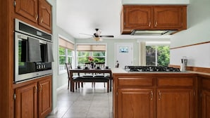 A kitchen with wooden cabinets, a stove, and a dining area with a table and chairs. - Summer Home near Long Lake with Hot Tub & Firepit (Traverse City)