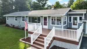 A two-story house with a porch, a flag, and a well-maintained lawn. - Summer Home near Long Lake with Hot Tub & Firepit (Traverse City)